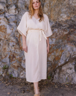 Femme se tenant devant un rocher portant une robe tunique beige en coton lin sous le soleil