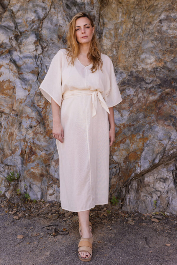 Femme se tenant devant un rocher portant une robe tunique beige en coton lin sous le soleil
