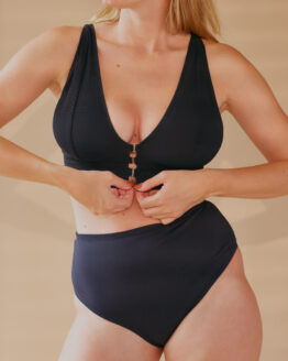 Femme se tenant debout portant un ensemble de lingerie en tulle stretch noir, ajustant son soutien gorge à l'aide d'attaches en crochet sur le devant