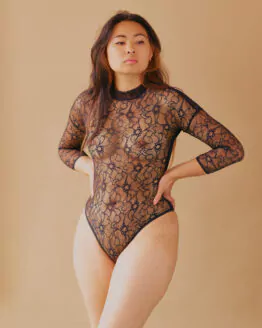 Femme debour portant un body en dentelle française noire, manches longues et col montant