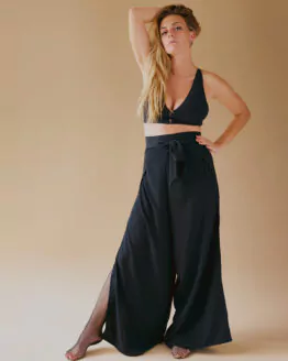 Femme debout se tenant les cheveux porte un petit top noir et un pantalon fendu noir avec des résilles