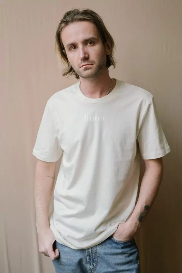 Homme portant un t-shirt écru manches courtes floqué Maison Finou à la coupe unisexe, droite et col rond